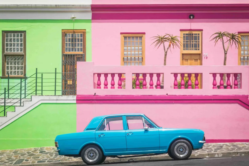 The blue car in front of the pink and green houses in Cape Town