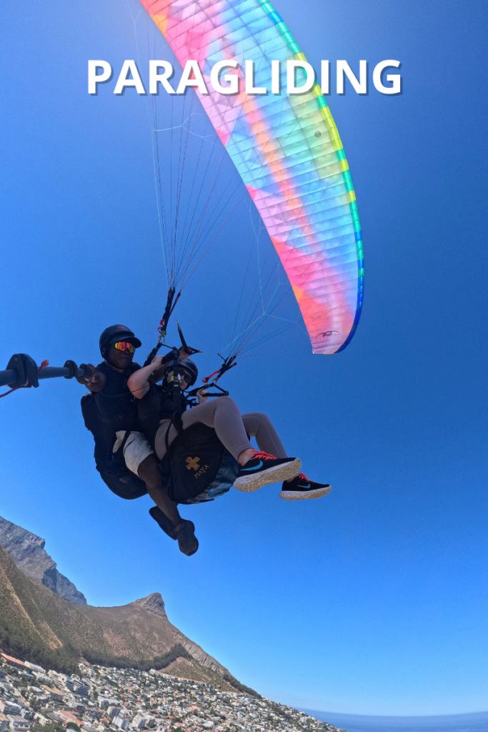 Photo of Hannah paragliding with Lion's Head in the background, white text at the top that reads "PARAGLIDING"